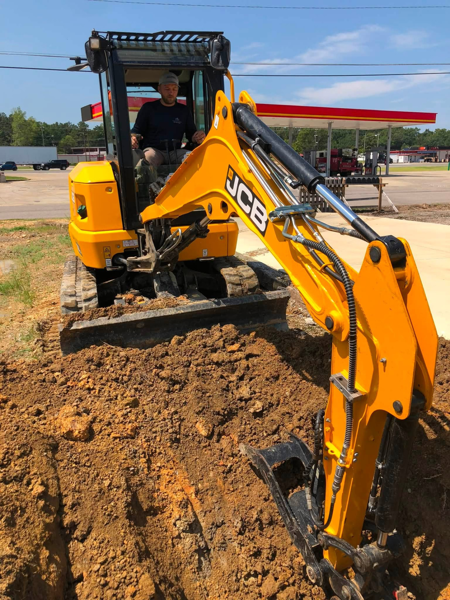 M&B Plumbing and Septic operator running a JCB mini-excavator trenching for a new sewer line in Gadsden, Alabama